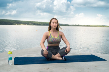 Young slim woman in sportswear practicing yoga near lake, nature