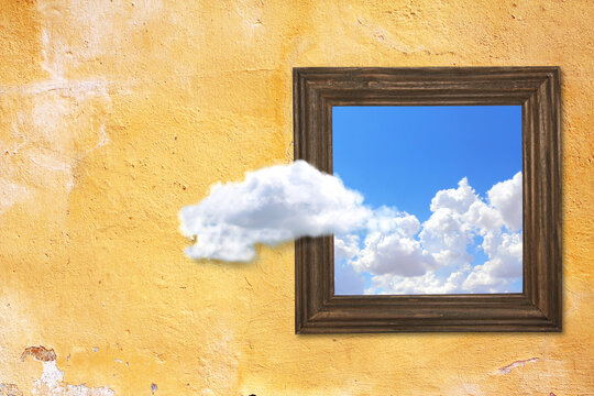 Wooden picture frame with photo of blue sky with clouds at brick wall background