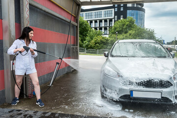 woman washes off the foam with water on the car, cleaning and washing the car