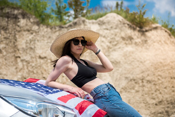Photo shoot of a charming lady with the USA flag near the car in a sand quarry