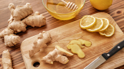 Preparation of cold and flu remedy cure drink, Close up of board, knife, fresh ginger, lemon, honey in a bowl with dipper on the wooden table