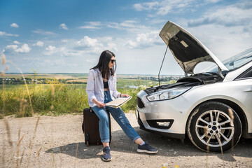 Young woman looks under the engine hood as broken cars motor. Car breakage in road