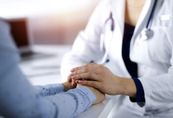 Unknown woman-doctor is holding her patient's hands, discussing current health examination, while...