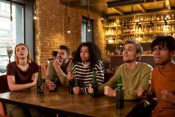 Friends looking worried and unhappy while watching sports match on TV together, drinking beer and cheering for team in the bar. People, leisure, friendship and entertainment concept