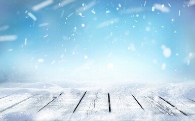 Beautiful winter snowy blurred defocused blue background and empty wooden flooring. Flakes of snow fall and sparkle on light, copy space.