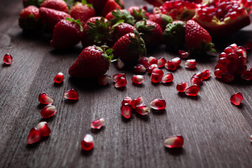strawberries and pomegranate seeds on a dark wooden background