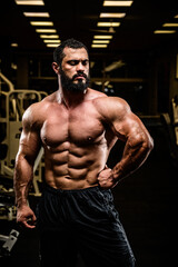 Fototapeta na wymiar handsome bearded young athlete man with strong muscular physique body in dark sport gym