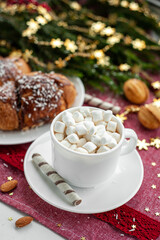 Christmas breakfast. Christmas morning. A cup of coffee or cocoa with marshmallows and sweets. On a red tablecloth next to a branch decorated with Christmas spruce. Selective focus.