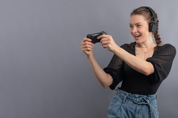 Happy excited gamer girl with joystick and headphones isolated on gray background. Gaming concept. Winner dance.