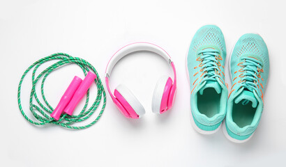 Sportive shoes, jumping rope and headphones on white background