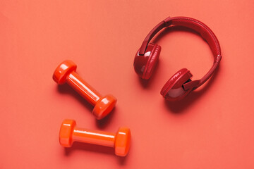 Dumbbells and headphones on color background