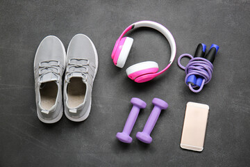 Sportive shoes, dumbbells, jumping rope, mobile phone and headphones on grey background