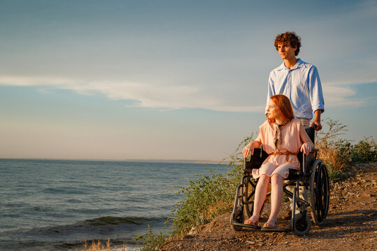 redhair woman in wheelchair talking with her partner by the sea at sunset
