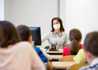 education, people and pandemic concept - group of children and teacher wearing face protective medical mask for protection from virus disease at school