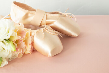 Pink ballet pointe shoes and a bouquet of delicate fresh flowers on a pink background.
