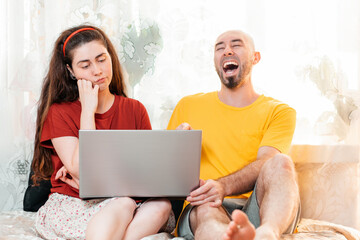 Emotions. A laughing man and a thoughtful woman look at their laptop together. The concept of family home stay