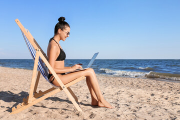 Beautiful young woman with laptop on sea beach