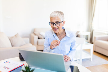 Woman wearing glasses at home concentrating as she works on a laptop. Middle-aged woman working...