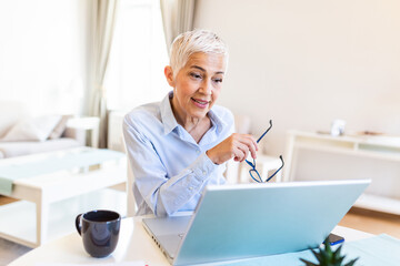 Elderly woman working on laptop computer, smiling. Woman Working From Home On Laptop In Modern Apartment. Trendy woman working on laptop from home