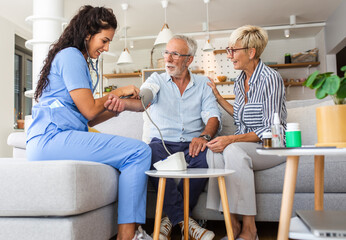 Fototapeta premium Female nurse measures blood pressure to seniors patients while being in a home visit.