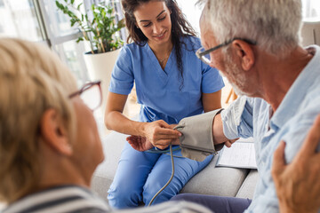 Female nurse measures blood pressure to seniors patients while being in a home visit.