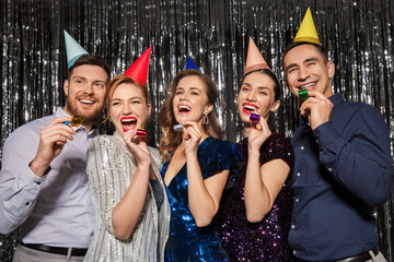 celebration, fun and holidays concept - happy couple with party blowers and birthday caps