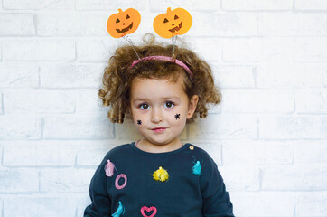 beautiful happy little girl in costume with pumpkin and painted spiders on her cheeks on light background. halloween kids