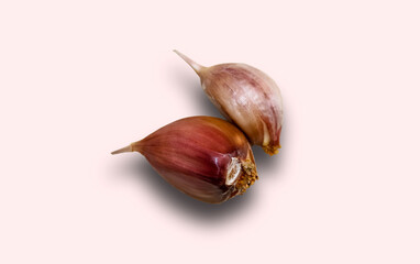 Two unpeeled garlic cloves on a light pink background with shadow. Close-up, selective shot.