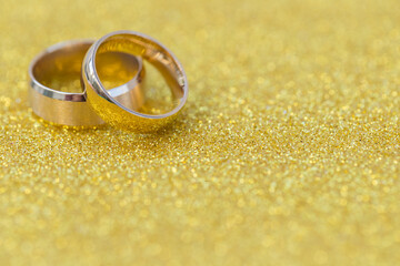Gold wedding rings of bride and groom on gold gliter