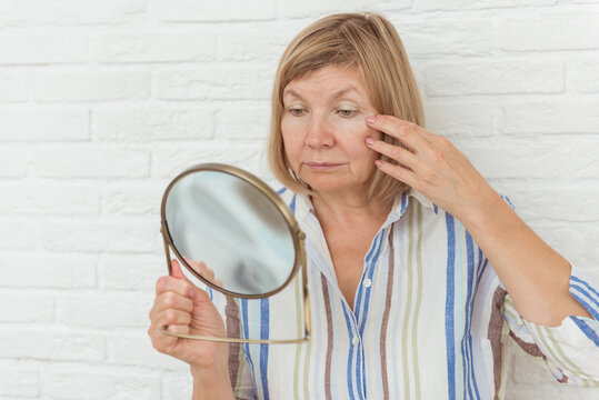 Elderly woman looking at wrinkled face in mirror