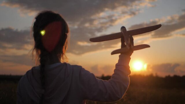 Cute girl playing with toy airplane in the wheat field at sunset. Silhouette of child playing with toy airplane on outdoor. Concept travel and freedom.