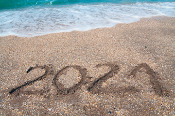 The inscription on the sand "2021" as a symbol of waiting and meeting the new year. The incoming sea wave.
