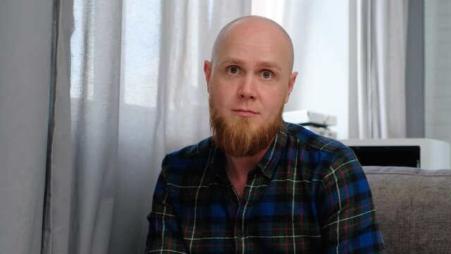 A young bald guy with a red beard gives an interview, emotionally telling a story while sitting comfortably on the couch. Serious, irritable, angry.