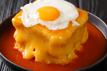 Delicious big Portuguese hot sandwich Francesinha with different types of sausages and meat, poured with cheese with tomato beer sauce and topped with a fried egg