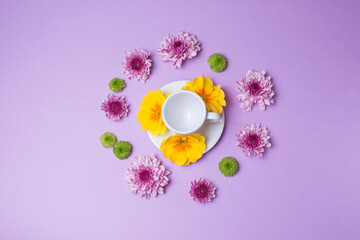 Obraz na płótnie Canvas Cup of espresso surrounded by flowers on purple background
