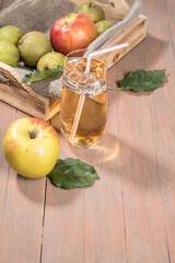 Apple and pear juice in a glass, apples and pears on a wooden tray with a napkin, Apple leaves and an Apple lie side by side, colored wooden background. A place for a space mine..Vertical orientation