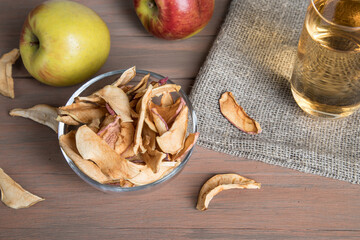 Apple chips in a glass plate, apples, a glass of Apple juice on a napkin, on a colored wooden background. Close up.The concept of a healthy snack. Horizontal orientation