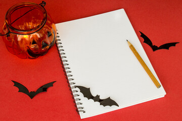 Halloween notepad. Pumpkin lantern, pen, bats and notepad on a red background. Traditional...