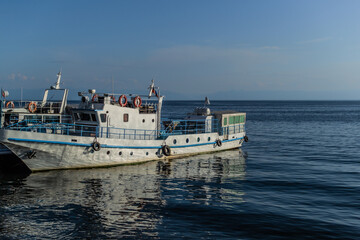 Fototapeta premium white vessel ship boat with blue stripes on pier in bay of lake baikal in the light of the sun with reflections in water, horizon
