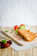 Butterfly ebi furai shrimp served with tomato and lettuce on a wooden chopping board along with ketchup