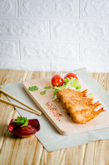 Butterfly ebi furai shrimp served with tomato and lettuce on a wooden chopping board along with ketchup