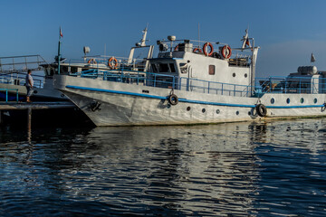 white ship boat with blue stripes on the pier in bay of lake Baikal in the light of sun with reflections