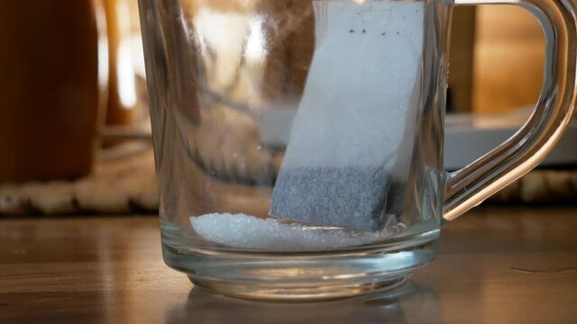 Taking electric ketle and pouring water inside a glass cup with sugar and tea bag for tea preparation. Home cooking