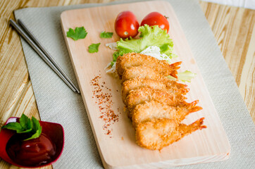 Butterfly ebi furai shrimp served with tomato and lettuce on a wooden chopping board along with ketchup