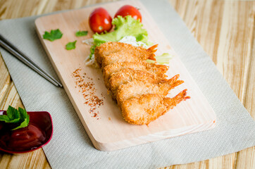 Butterfly ebi furai shrimp served with tomato and lettuce on a wooden chopping board along with ketchup