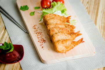 Butterfly ebi furai shrimp served with tomato and lettuce on a wooden chopping board along with ketchup