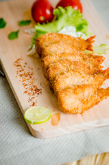 Butterfly ebi furai shrimp served with tomato and lettuce on a wooden chopping board along with ketchup
