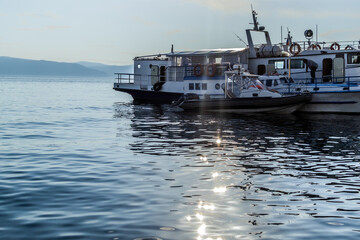 Naklejka premium white ships boats on pier in bay of blue lake baikal with glowing and reflections in water in light of sunset