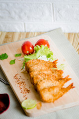 Butterfly ebi furai shrimp served with tomato and lettuce on a wooden chopping board along with ketchup