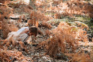 Little caucasian baby girl squatting in the forest among ferns